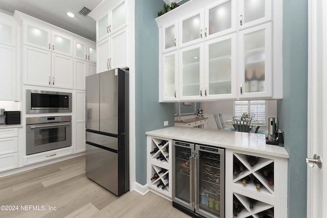 kitchen featuring wine cooler, light stone countertops, light wood-type flooring, appliances with stainless steel finishes, and white cabinetry