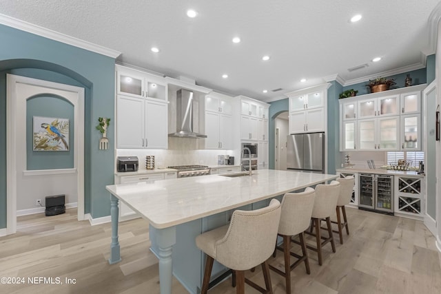 kitchen with wall chimney exhaust hood, stainless steel appliances, sink, white cabinets, and an island with sink