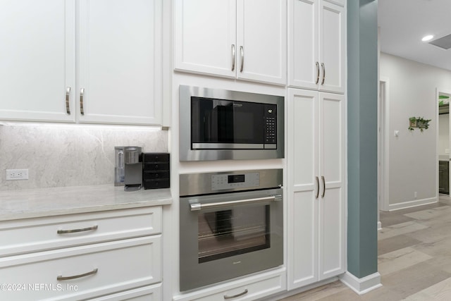 kitchen featuring tasteful backsplash, light stone counters, stainless steel appliances, light hardwood / wood-style flooring, and white cabinetry