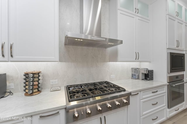 kitchen with decorative backsplash, stainless steel appliances, white cabinetry, and wall chimney exhaust hood