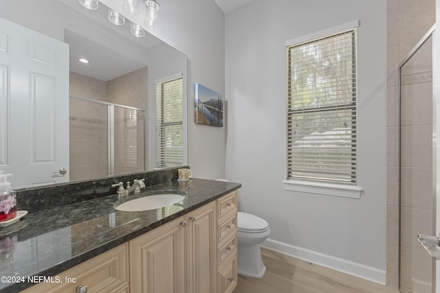 bathroom featuring vanity, a healthy amount of sunlight, hardwood / wood-style flooring, toilet, and a shower with shower door