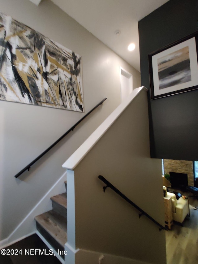 staircase with hardwood / wood-style floors and a stone fireplace