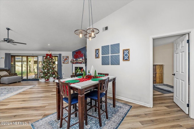 dining space featuring ceiling fan with notable chandelier, vaulted ceiling, and light hardwood / wood-style flooring