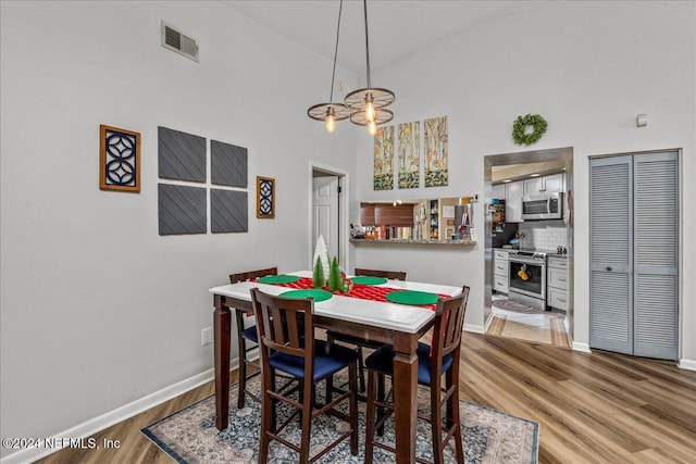 dining space featuring hardwood / wood-style flooring, high vaulted ceiling, and an inviting chandelier