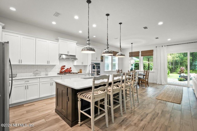 kitchen with white cabinets, stainless steel appliances, a center island with sink, and hanging light fixtures