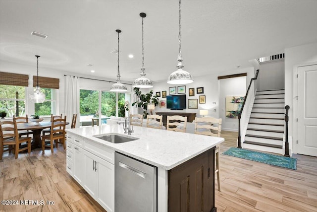 kitchen featuring a kitchen island with sink, dishwasher, white cabinets, and pendant lighting