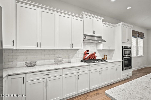 kitchen with tasteful backsplash, white cabinets, stainless steel appliances, and light wood-type flooring