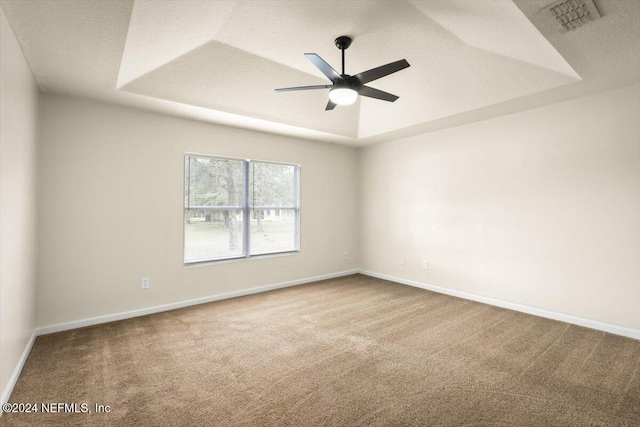 spare room with a textured ceiling, carpet floors, a tray ceiling, and ceiling fan