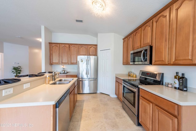 kitchen with an island with sink, a sink, light countertops, appliances with stainless steel finishes, and brown cabinets