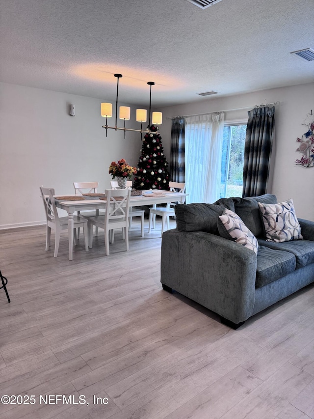 living room featuring light hardwood / wood-style floors, a textured ceiling, and an inviting chandelier