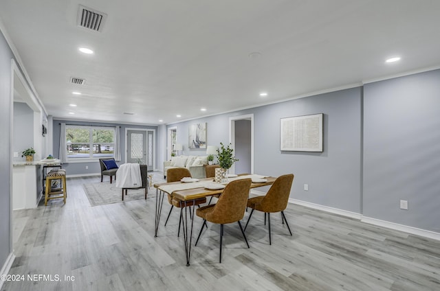 dining space with ornamental molding and light hardwood / wood-style flooring