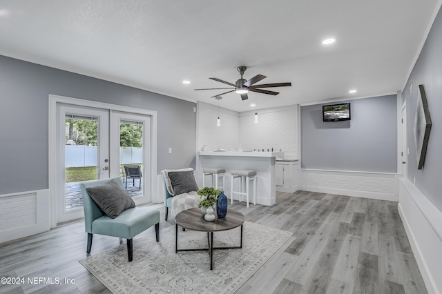 sitting room with ceiling fan, french doors, ornamental molding, and light wood-type flooring