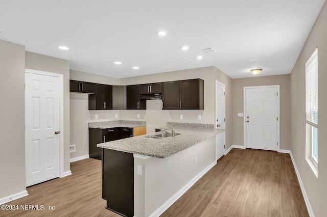 kitchen with light stone countertops, sink, light hardwood / wood-style flooring, kitchen peninsula, and dark brown cabinets