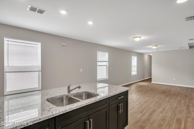 kitchen with dark brown cabinetry, light stone countertops, sink, and light hardwood / wood-style flooring