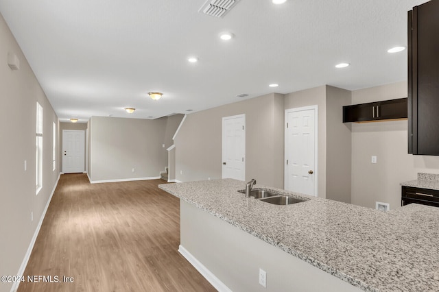 kitchen with light stone counters, dark brown cabinetry, sink, and light hardwood / wood-style flooring