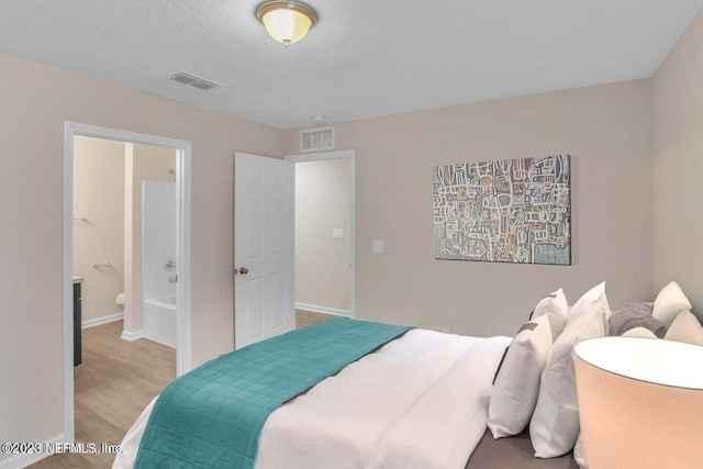 bedroom with connected bathroom, a textured ceiling, and light wood-type flooring