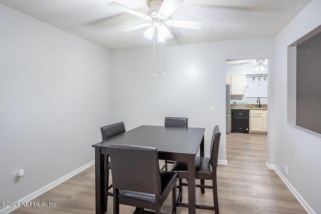 dining space featuring a textured ceiling, ceiling fan, sink, and light hardwood / wood-style flooring