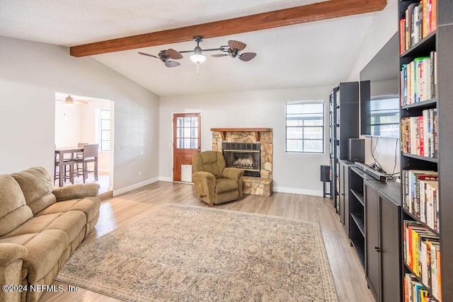 living room featuring lofted ceiling with beams, light hardwood / wood-style floors, and a stone fireplace