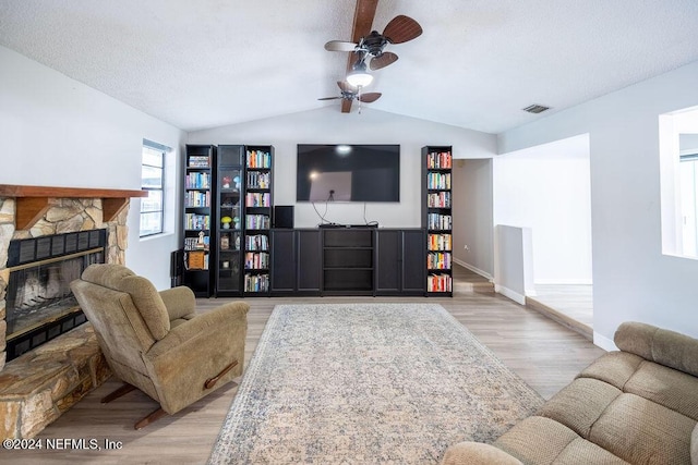 living room with vaulted ceiling with beams, ceiling fan, a fireplace, and light wood-type flooring