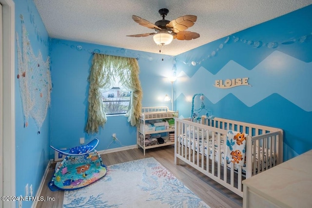 bedroom featuring hardwood / wood-style flooring, ceiling fan, a textured ceiling, and a nursery area