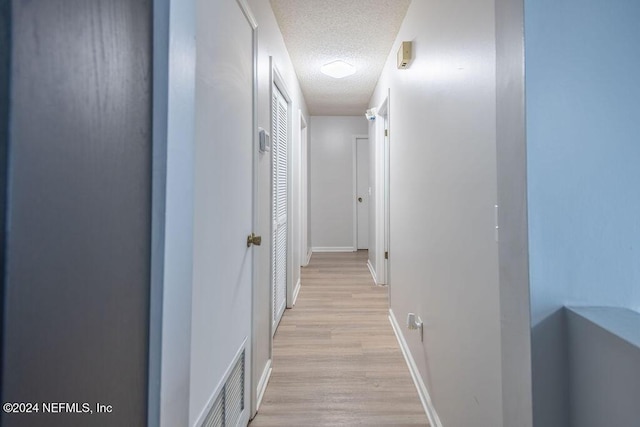 hall with a textured ceiling and light hardwood / wood-style floors