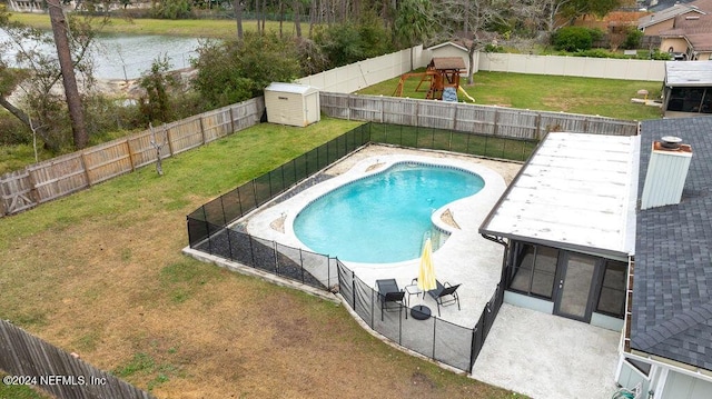 view of swimming pool featuring a water view, a yard, and a storage shed