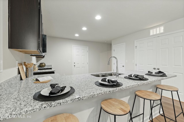 kitchen featuring sink, a kitchen breakfast bar, light stone counters, light hardwood / wood-style flooring, and kitchen peninsula