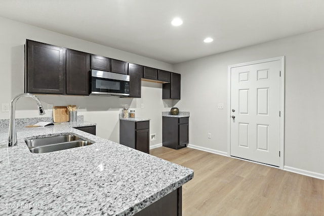 kitchen with dark brown cabinetry, light stone counters, light hardwood / wood-style flooring, and sink