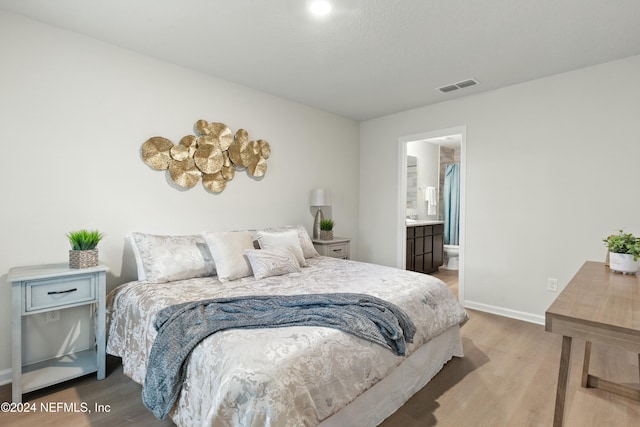 bedroom with ensuite bath and hardwood / wood-style flooring