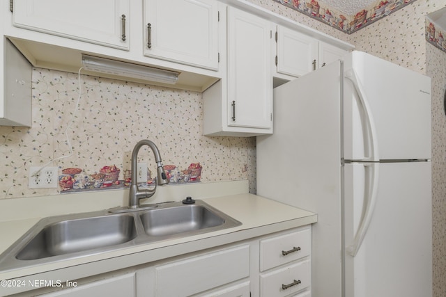 kitchen featuring decorative backsplash, white refrigerator, white cabinetry, and sink