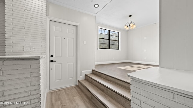 entryway with wood walls, light wood-type flooring, crown molding, and an inviting chandelier