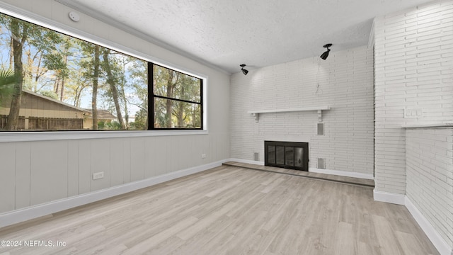 unfurnished living room with a fireplace, brick wall, a textured ceiling, and light hardwood / wood-style floors