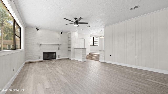 unfurnished living room with ceiling fan with notable chandelier, a textured ceiling, light hardwood / wood-style flooring, and a brick fireplace