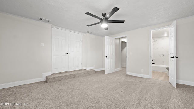 unfurnished bedroom featuring a textured ceiling, ceiling fan, ensuite bathroom, and a closet