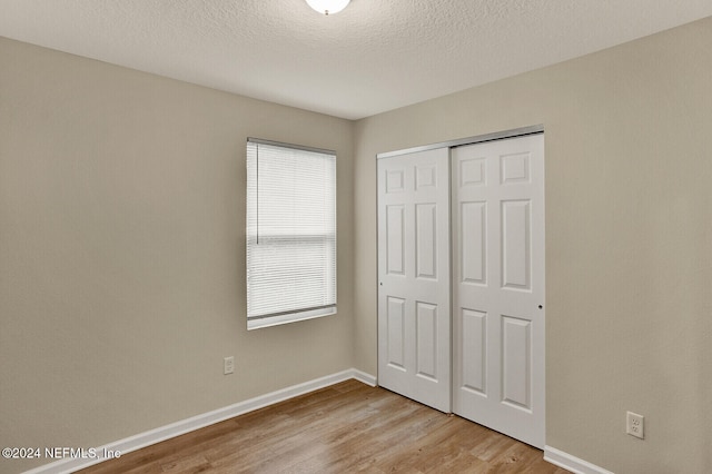 unfurnished bedroom with a textured ceiling, light wood-type flooring, and a closet