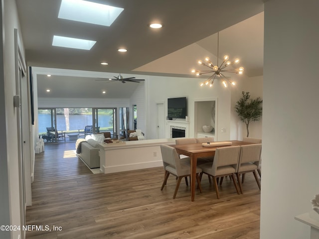 dining area featuring wood-type flooring, ceiling fan with notable chandelier, and vaulted ceiling with skylight