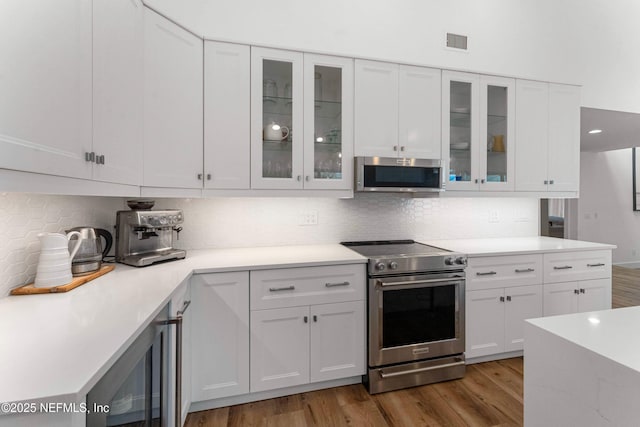 kitchen with wood-type flooring, appliances with stainless steel finishes, white cabinets, and backsplash