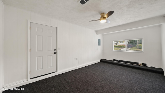 empty room featuring carpet, a textured ceiling, ceiling fan, wooden walls, and electric panel