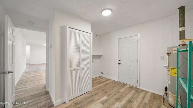 corridor with a textured ceiling, light hardwood / wood-style flooring, and gas water heater