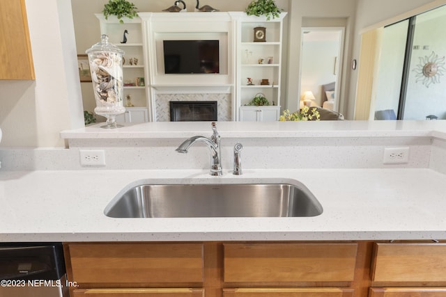 kitchen with a high end fireplace, light stone countertops, dishwasher, and sink