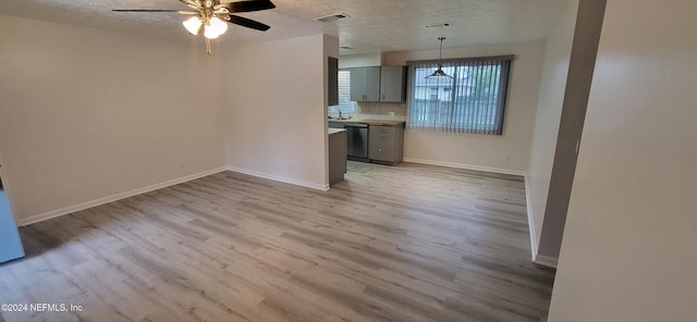 unfurnished living room with a textured ceiling, light wood-type flooring, ceiling fan, and sink