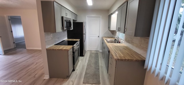 kitchen with gray cabinetry, sink, stainless steel appliances, wood counters, and tasteful backsplash