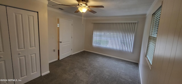 unfurnished bedroom featuring a closet, dark carpet, ceiling fan, and crown molding