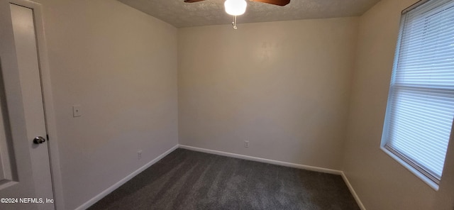 spare room featuring a textured ceiling, dark carpet, and ceiling fan