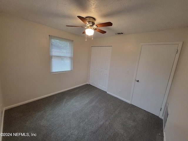 unfurnished bedroom featuring dark colored carpet, ceiling fan, a textured ceiling, and a closet