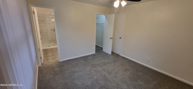 unfurnished bedroom featuring ceiling fan, a spacious closet, ensuite bathroom, a closet, and dark carpet