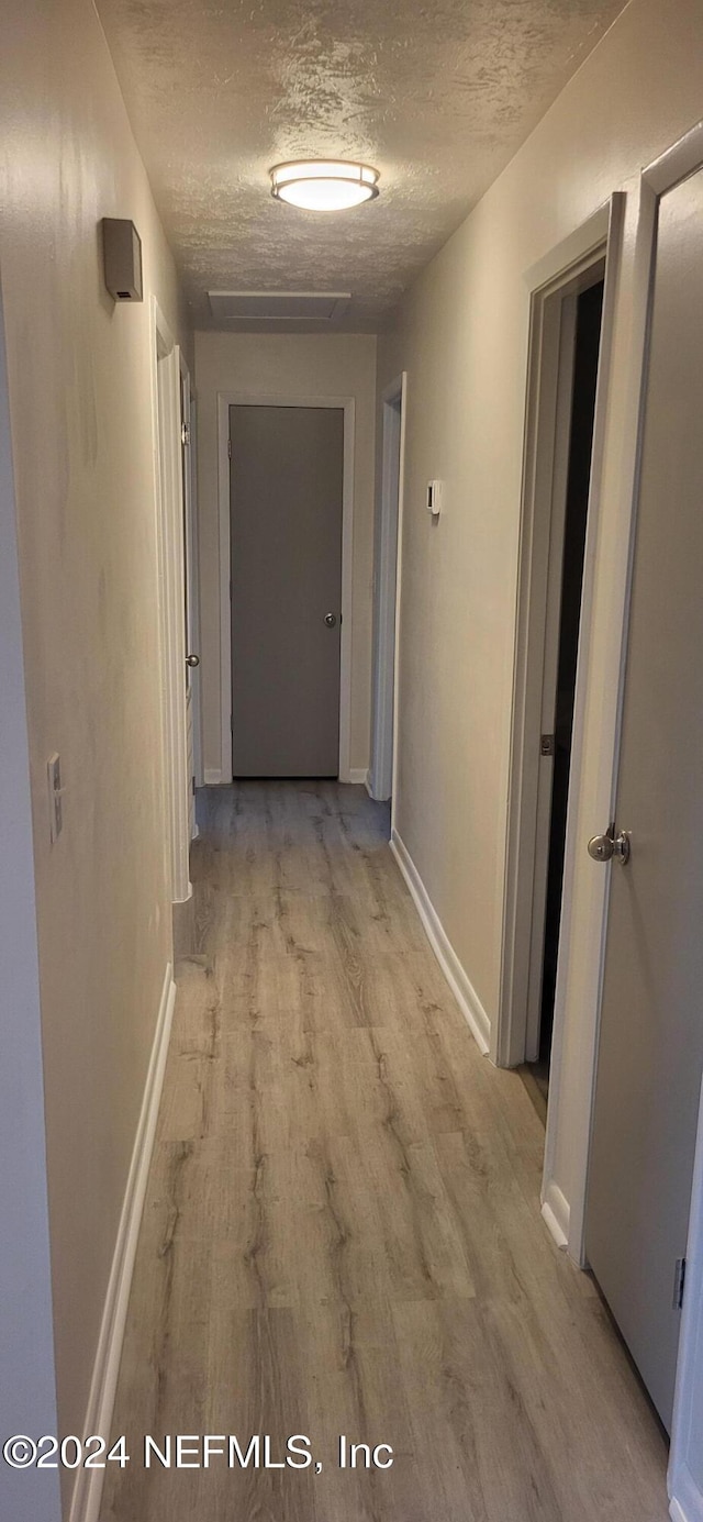 hall with light wood-type flooring and a textured ceiling