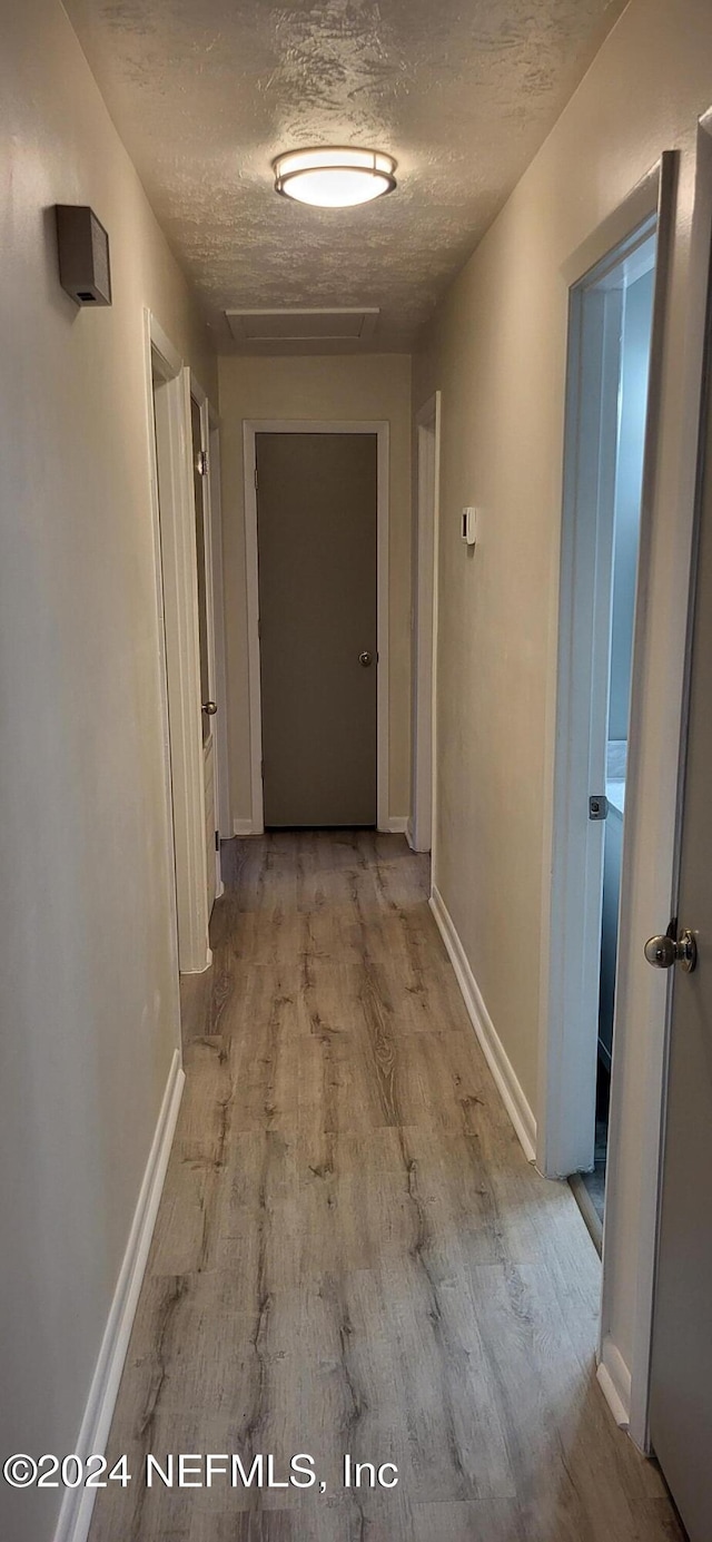 hallway featuring light hardwood / wood-style floors and a textured ceiling