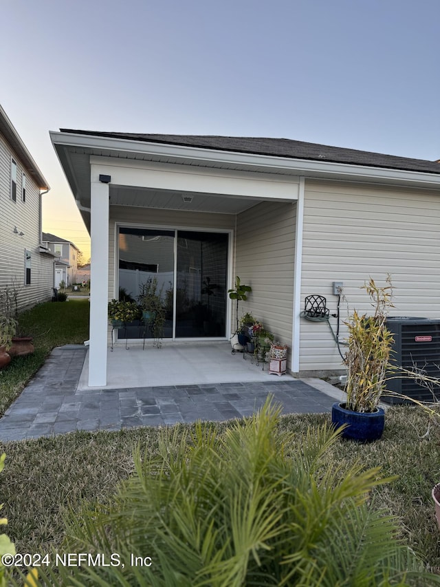 back house at dusk featuring central air condition unit and a patio area