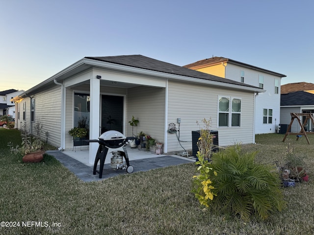 back house at dusk featuring a yard, cooling unit, and a patio area